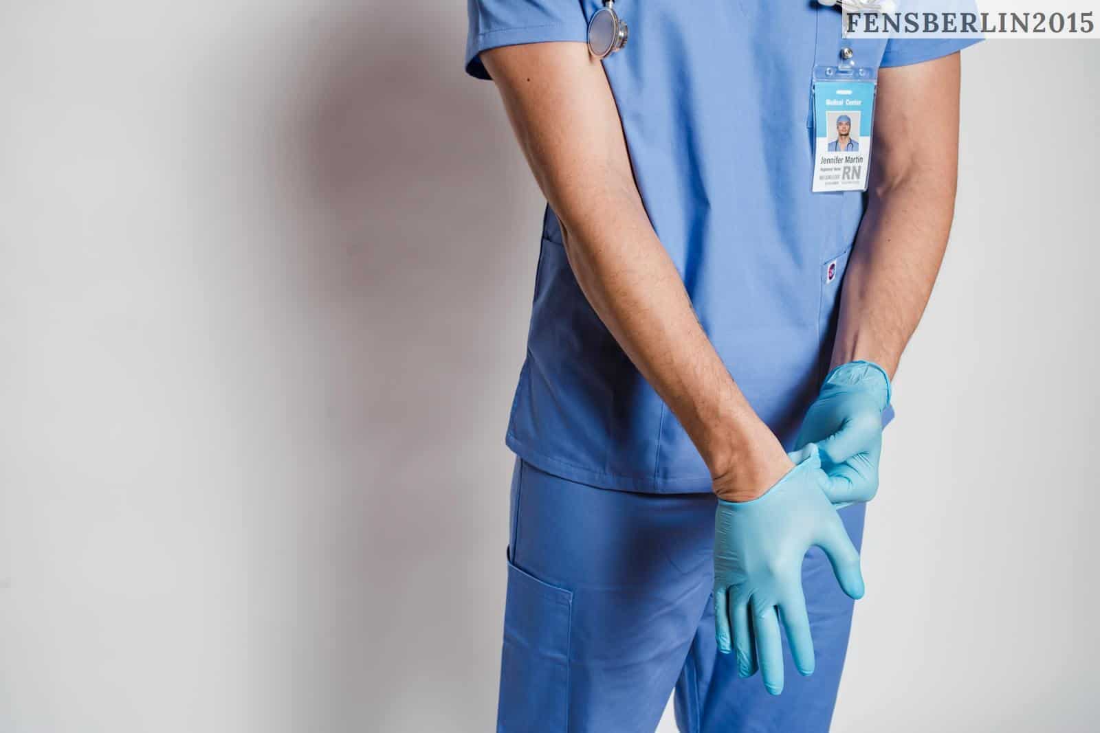 Crop anonymous male doctor in uniform with stethoscope putting on sterile gloves while standing near white wall in hospital